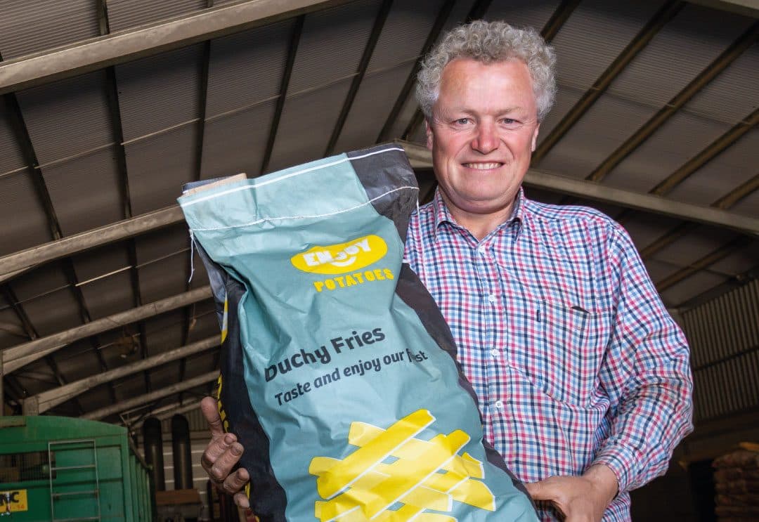 Farmer in a barn holding a bag of Duchy Fries potatoes