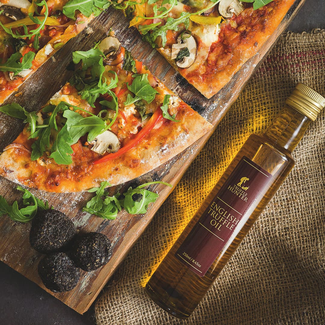 Bottle of English truffle oil beside pizza slices and whole black truffles