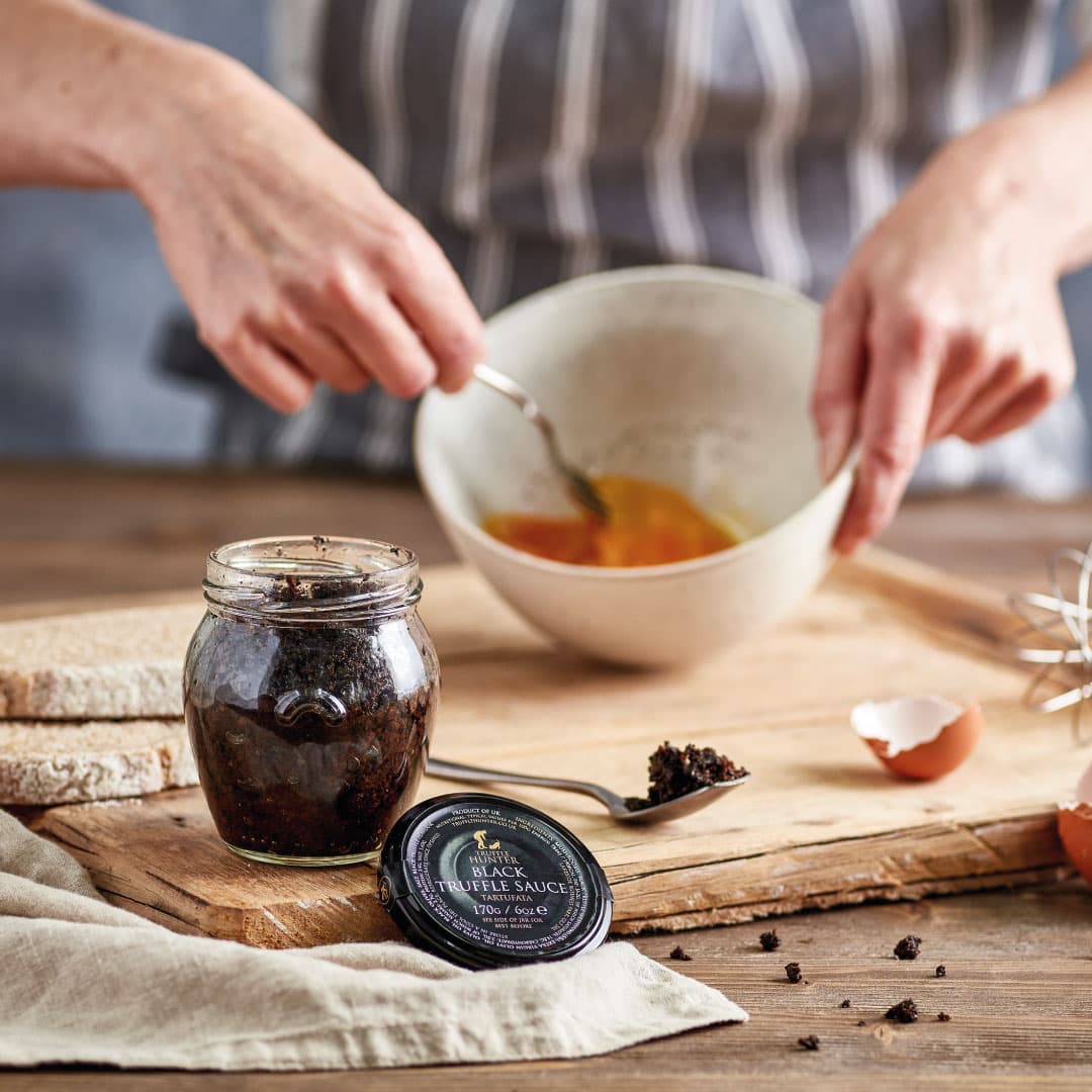 Jar of black truffle sauce beside a cook whisking eggs in a bowl