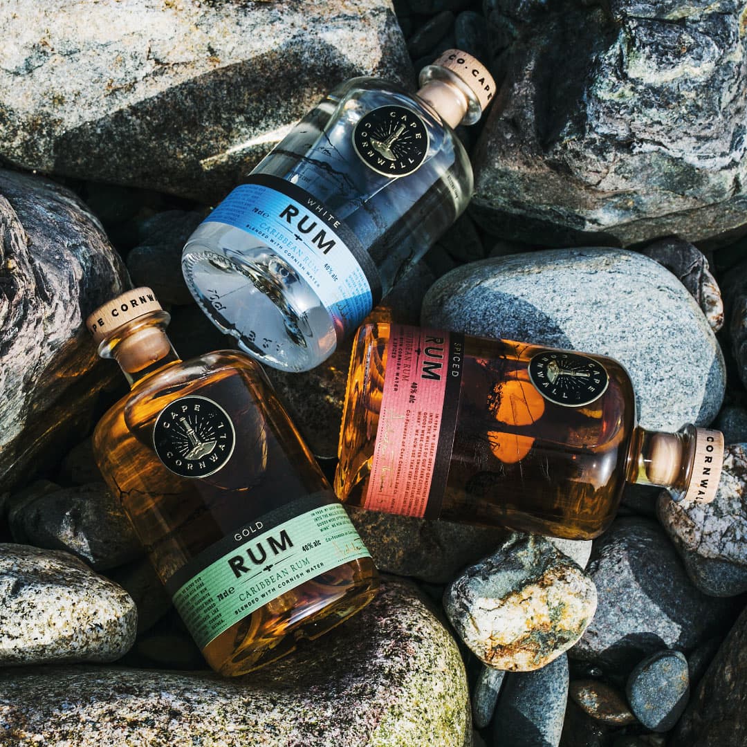 Three bottles of Cornish white, gold and spiced rum lying on beach pebbles