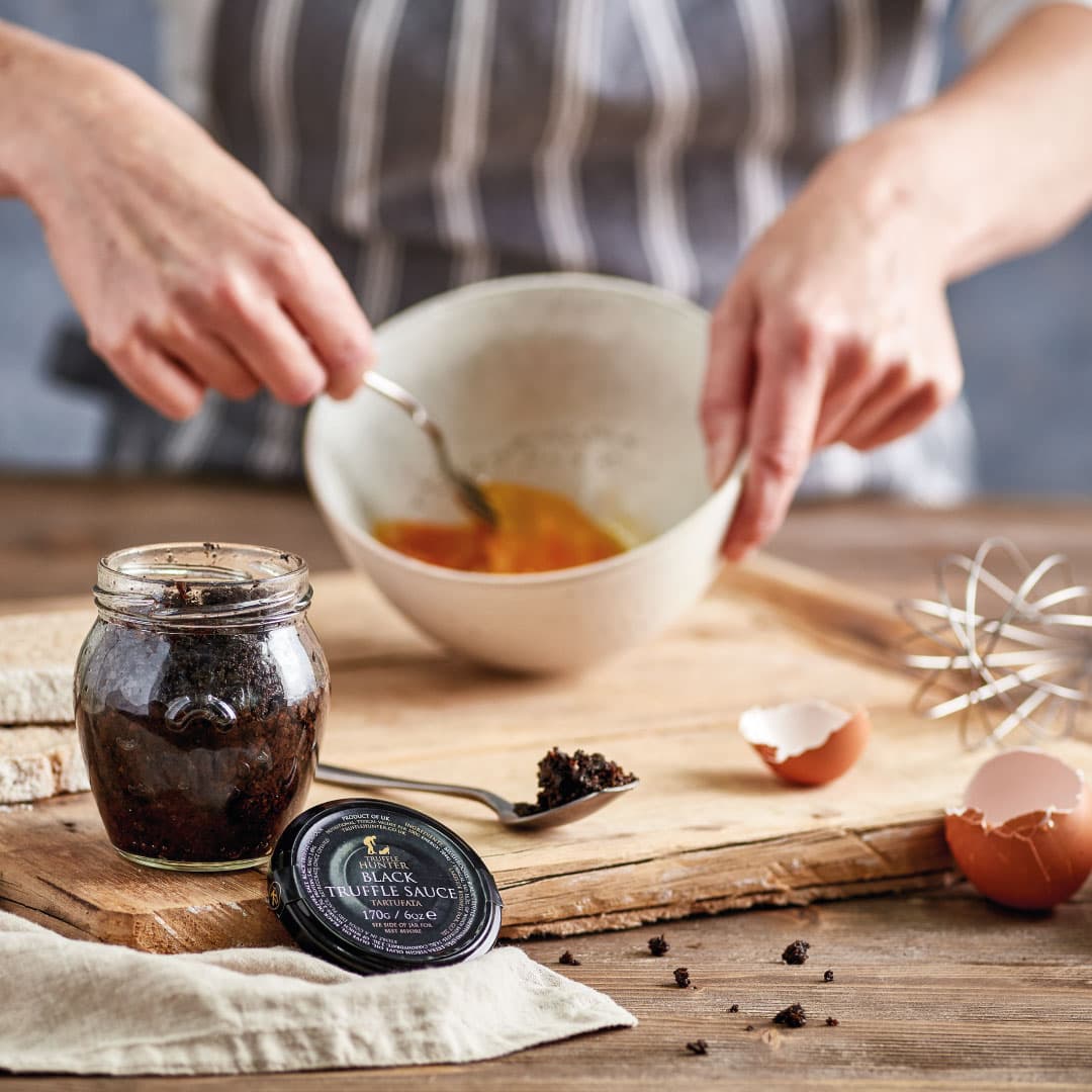 Jar of black truffle sauce as a cook whisks eggs in a bowl