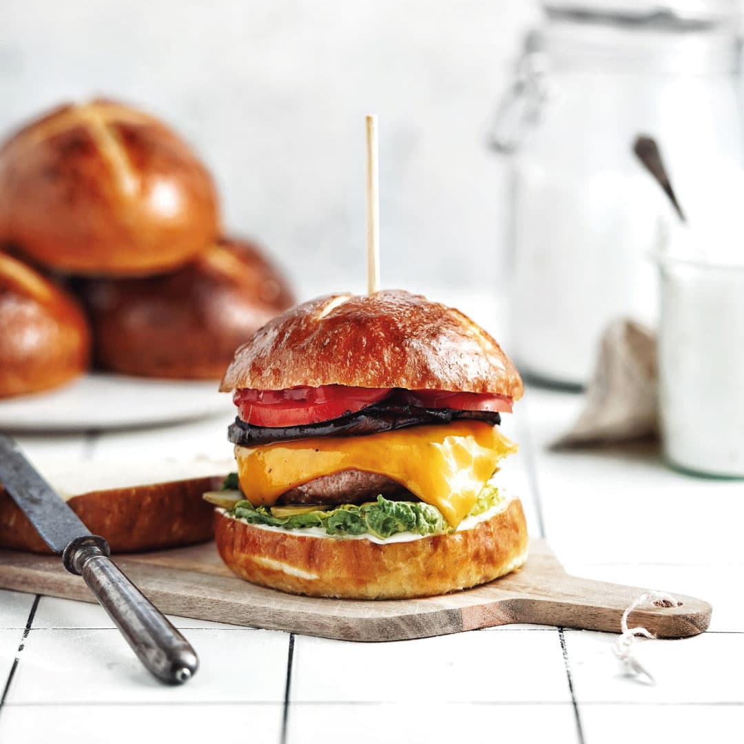 Burger with melted plant-based cheese, tomato and aubergine in a pretzel bun