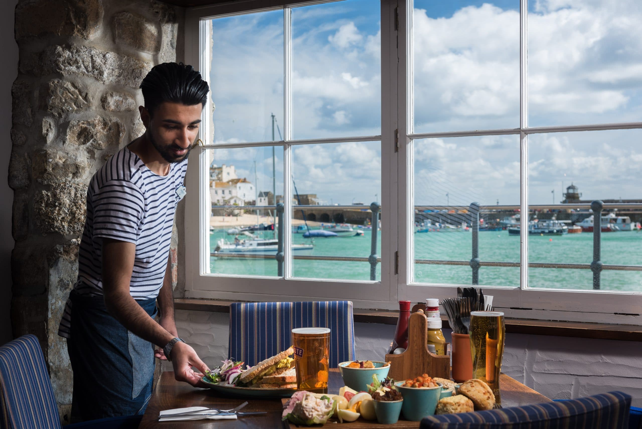 Waiter serving food at a window table overlooking a harbour