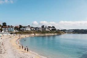 Sandy Cornish beach and calm blue bay with seaside houses on the cliff
