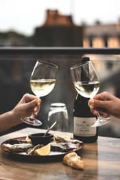 Two glasses of white wine raised over a plate of oysters
