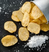 Crisps spilling from a metal pail beside sea salt flakes