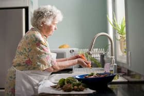 Older woman washing fresh carrots at a kitchen sink