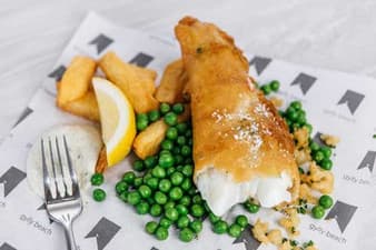 Battered fish with chips, peas, lemon and tartare sauce on branded paper
