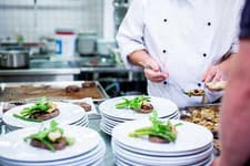 Chef plating starters on rows of stacked white plates in a busy kitchen
