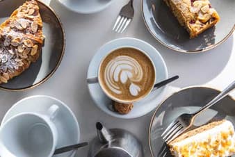 Latte art coffee with almond croissant and cakes on a café table