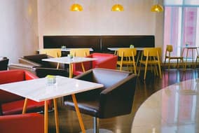 Café interior with red and brown chairs, white tables and yellow pendant lights