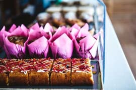 Muffins in pink cases and iced traybake slices in a café display counter