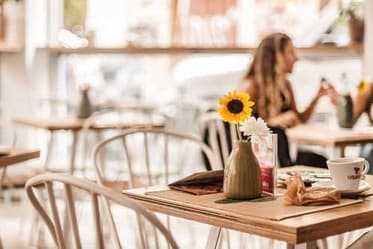 Café table with a sunflower vase and coffee cup, diners in the background