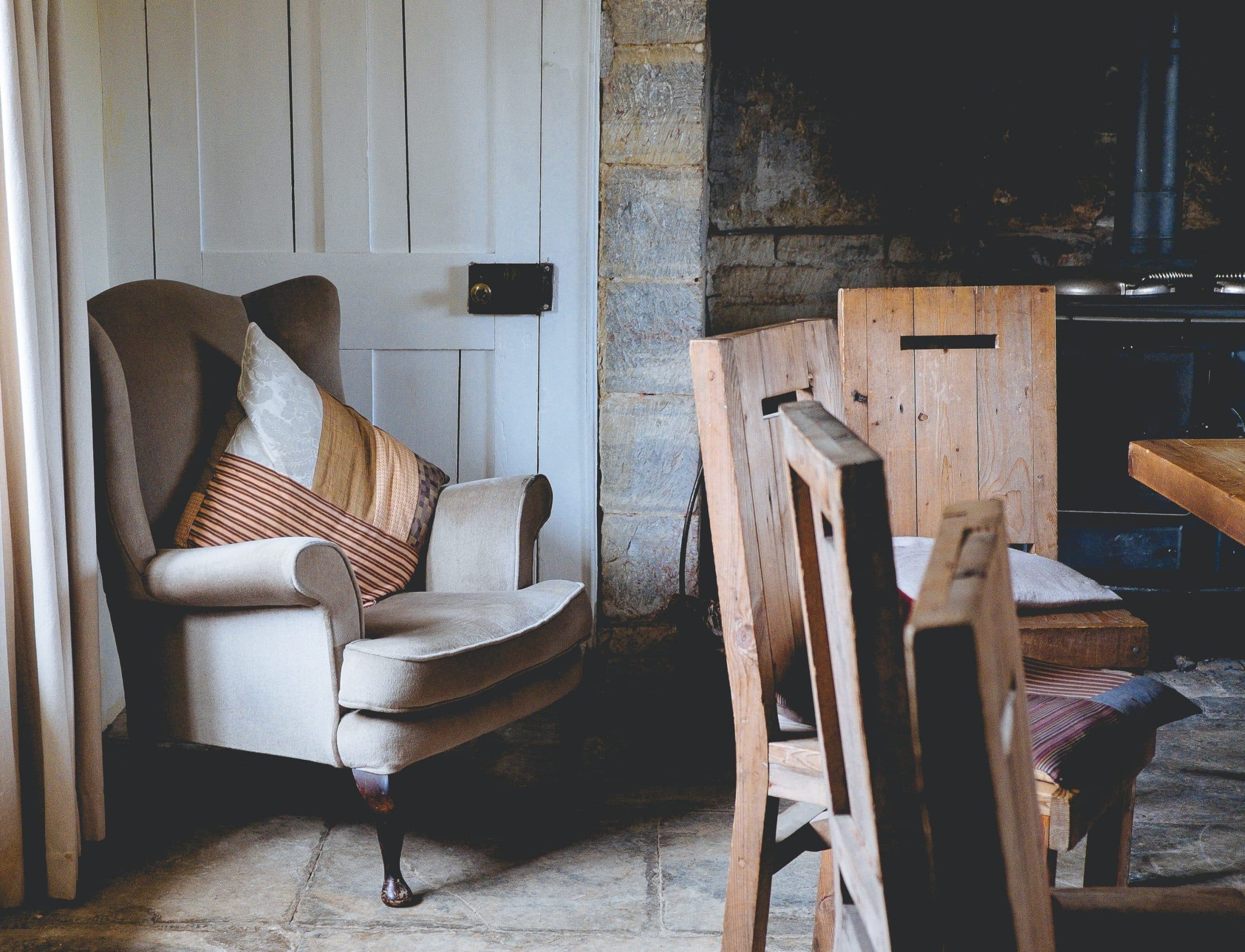 Cosy inn interior with an armchair, stone wall and wooden dining chairs