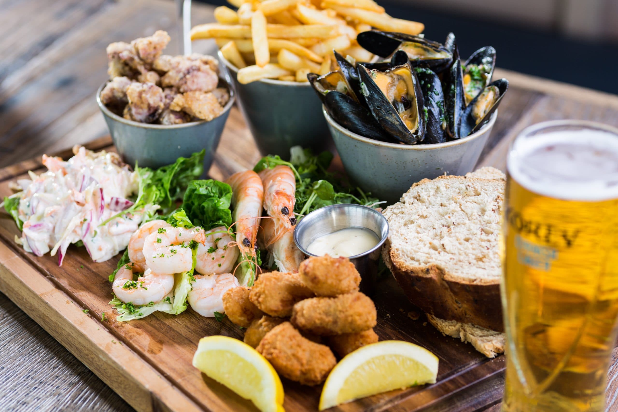 Seafood sharing board with mussels, prawns, calamari, chips and a pint