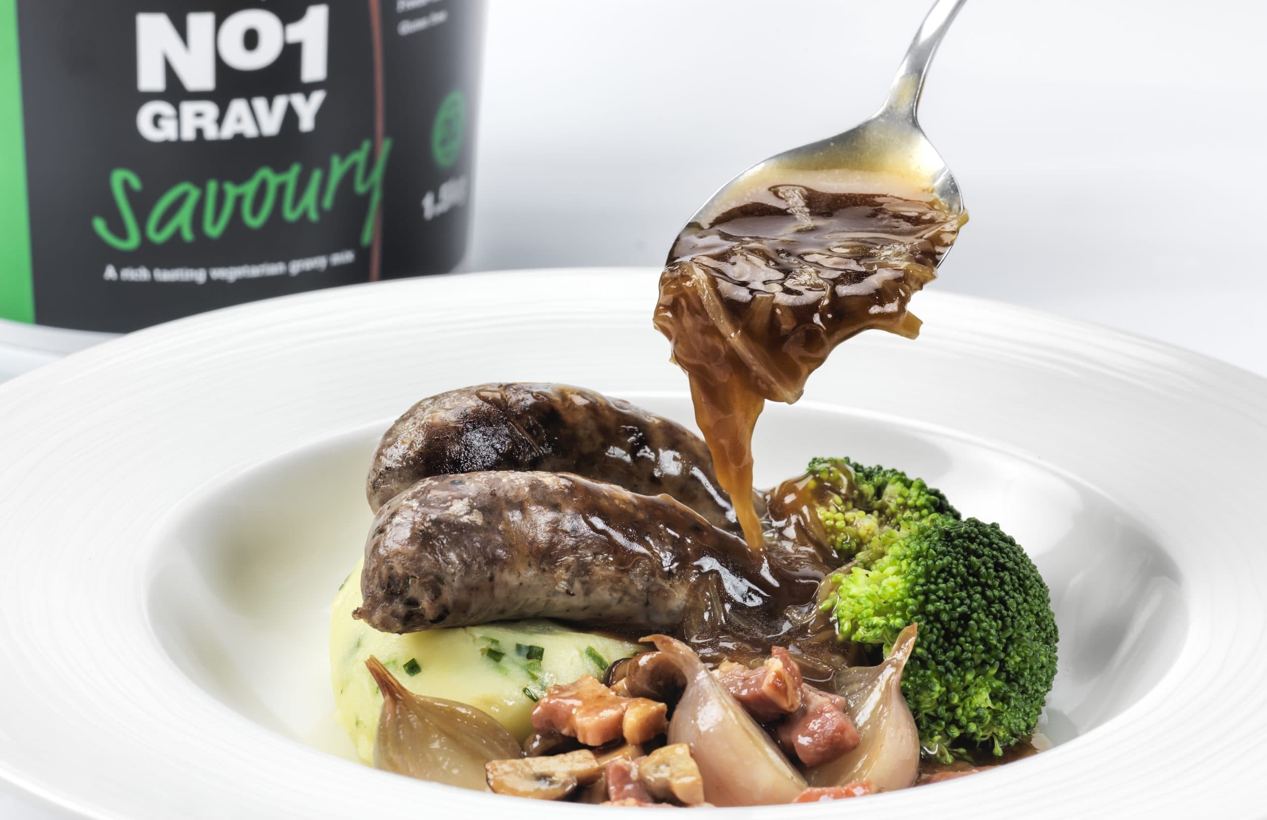 Gravy poured over sausages, mash and broccoli