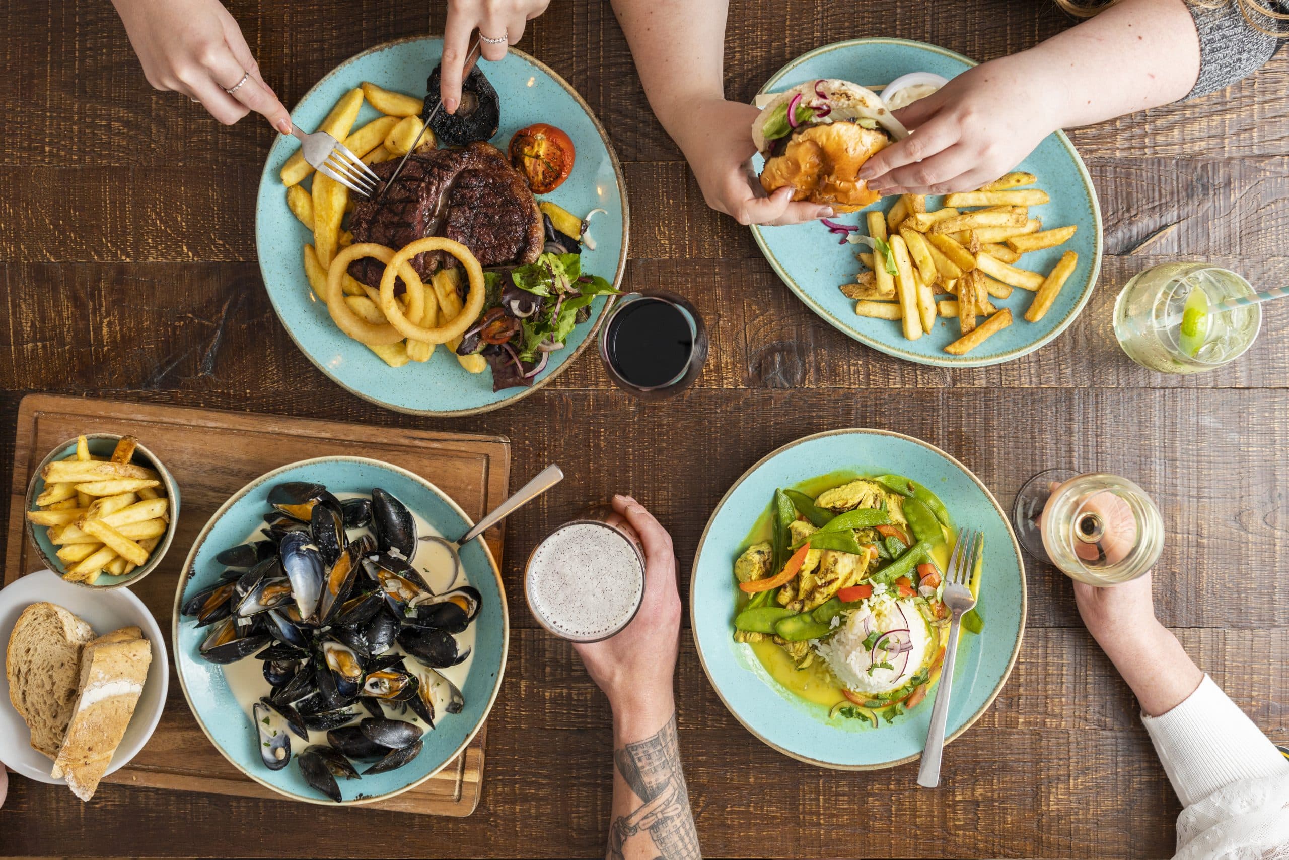 Diners sharing steak, mussels, curry and chips around a wooden table