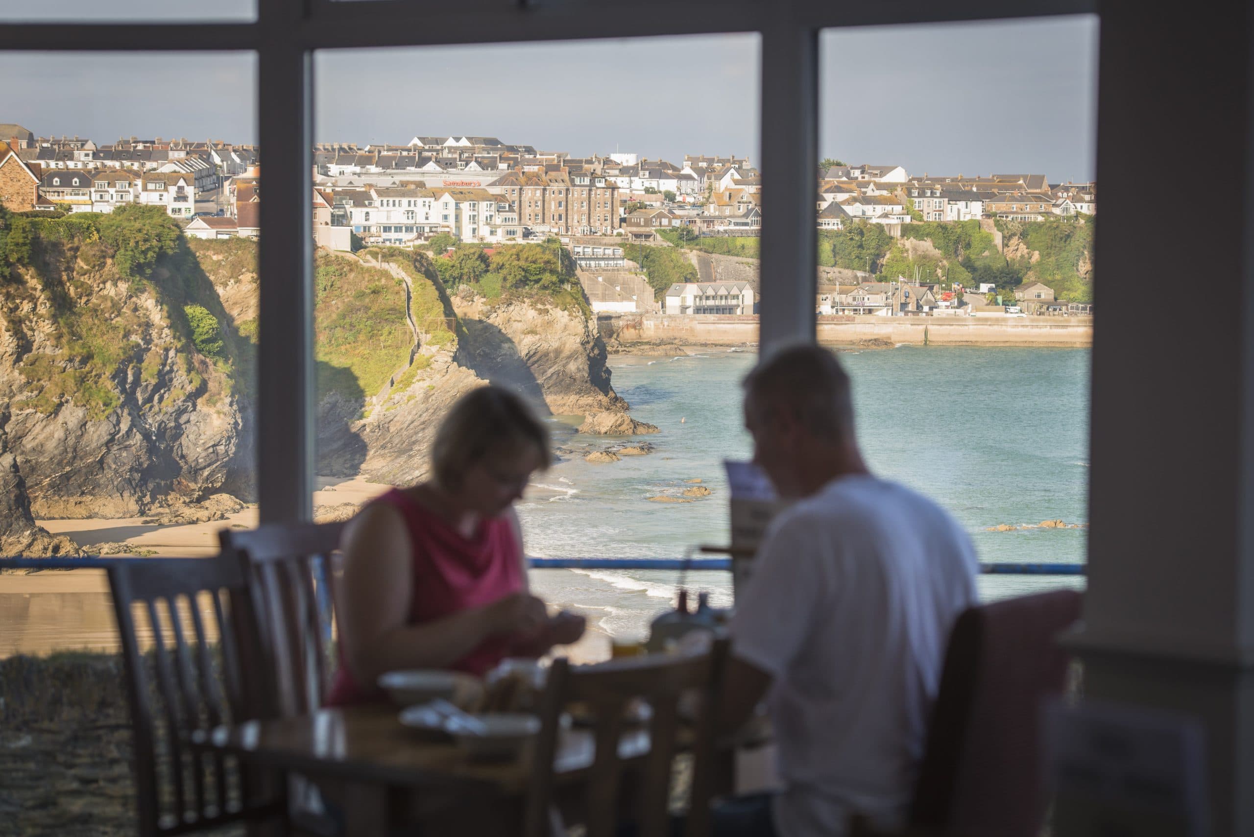 Couple dining by a window overlooking a beach and coastal town