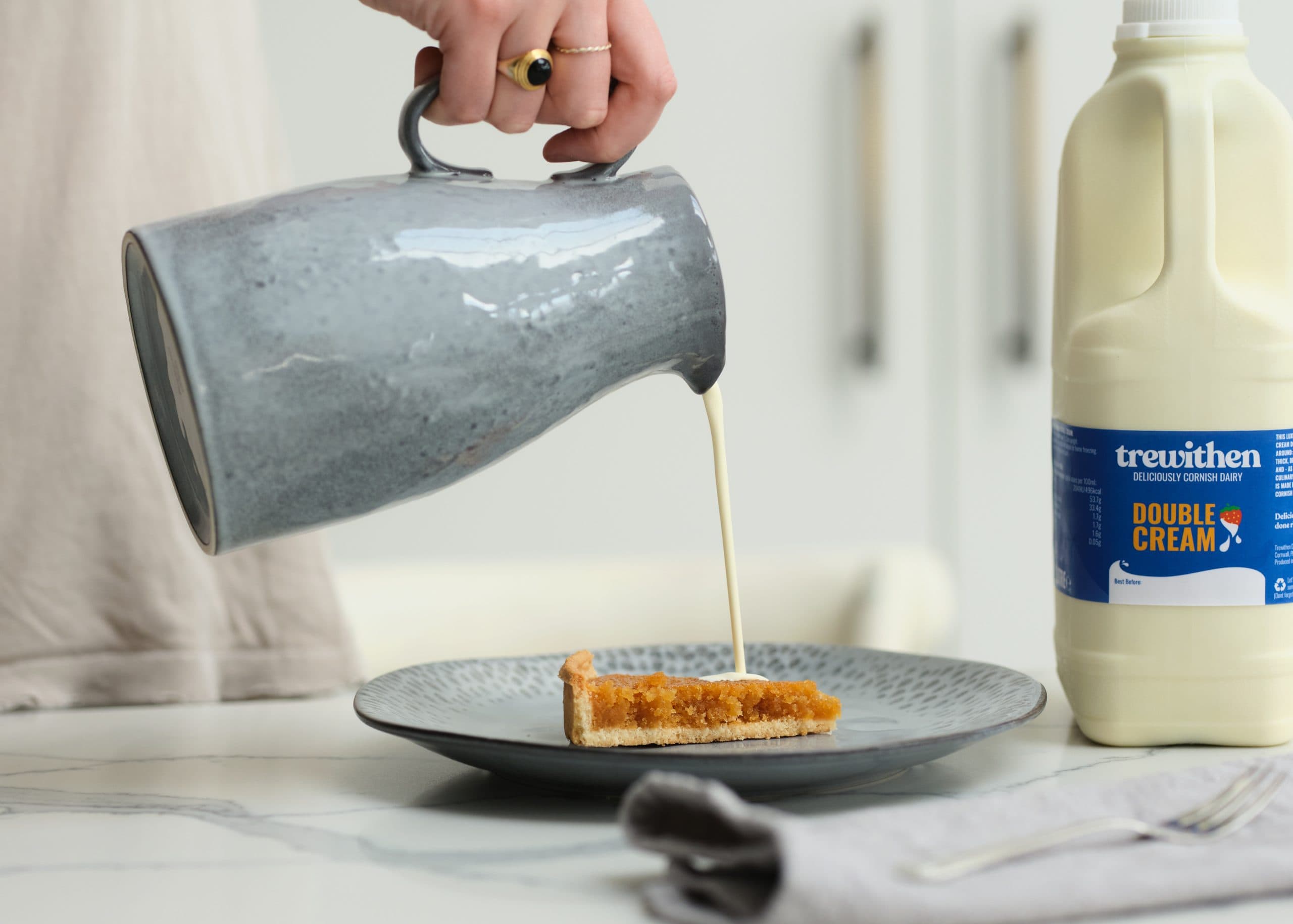 Cream poured over a tart slice beside Trewithen double cream