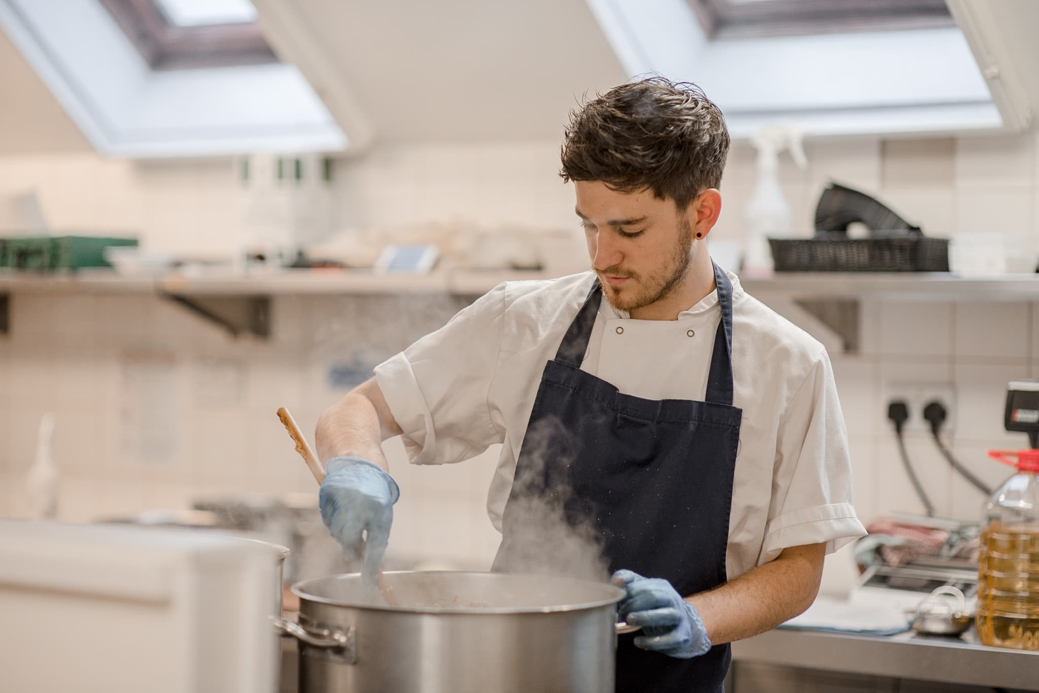 Young chef in an apron stirring a steaming stockpot in a kitchen