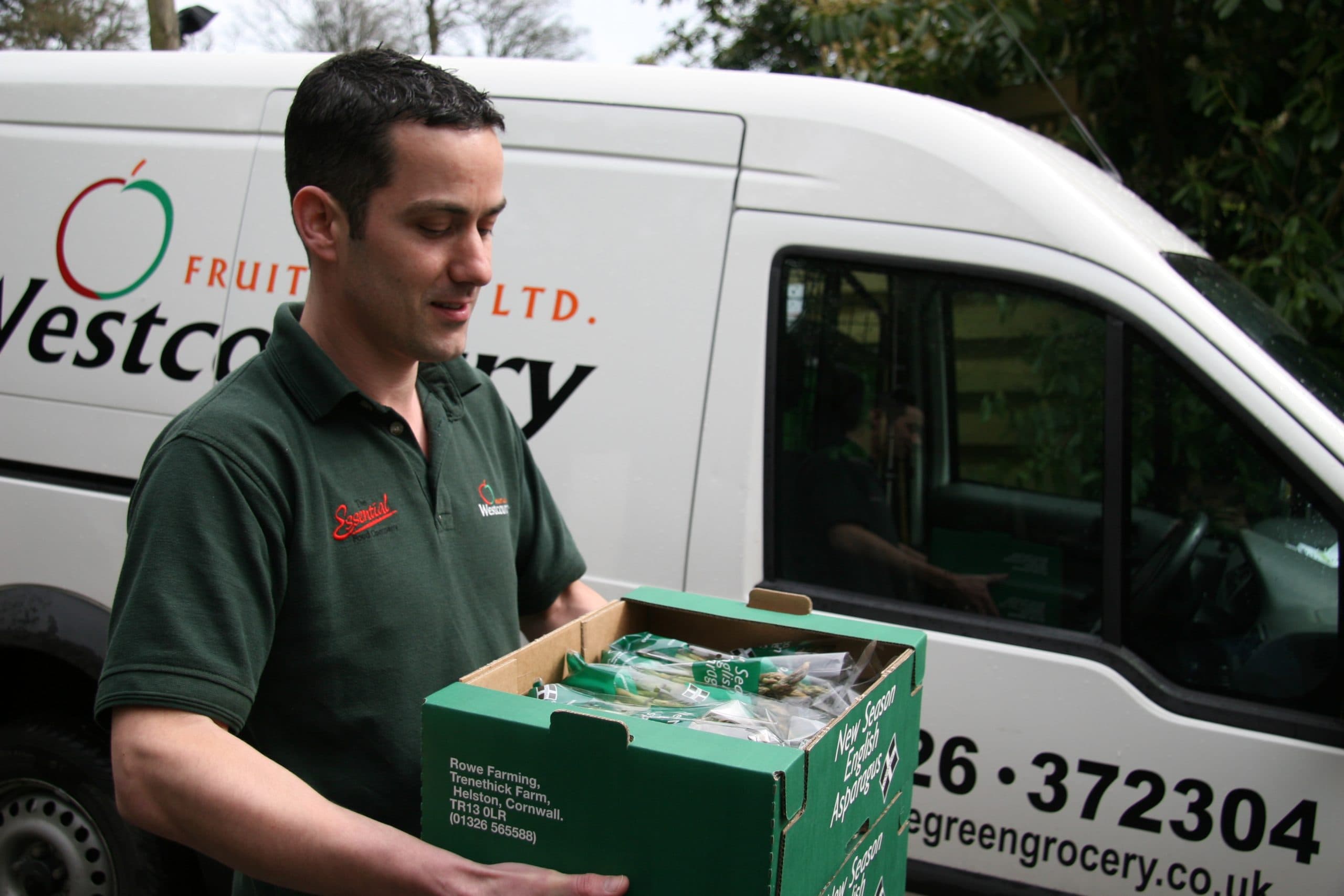 Westcountry driver carrying a box of fresh produce from a delivery van