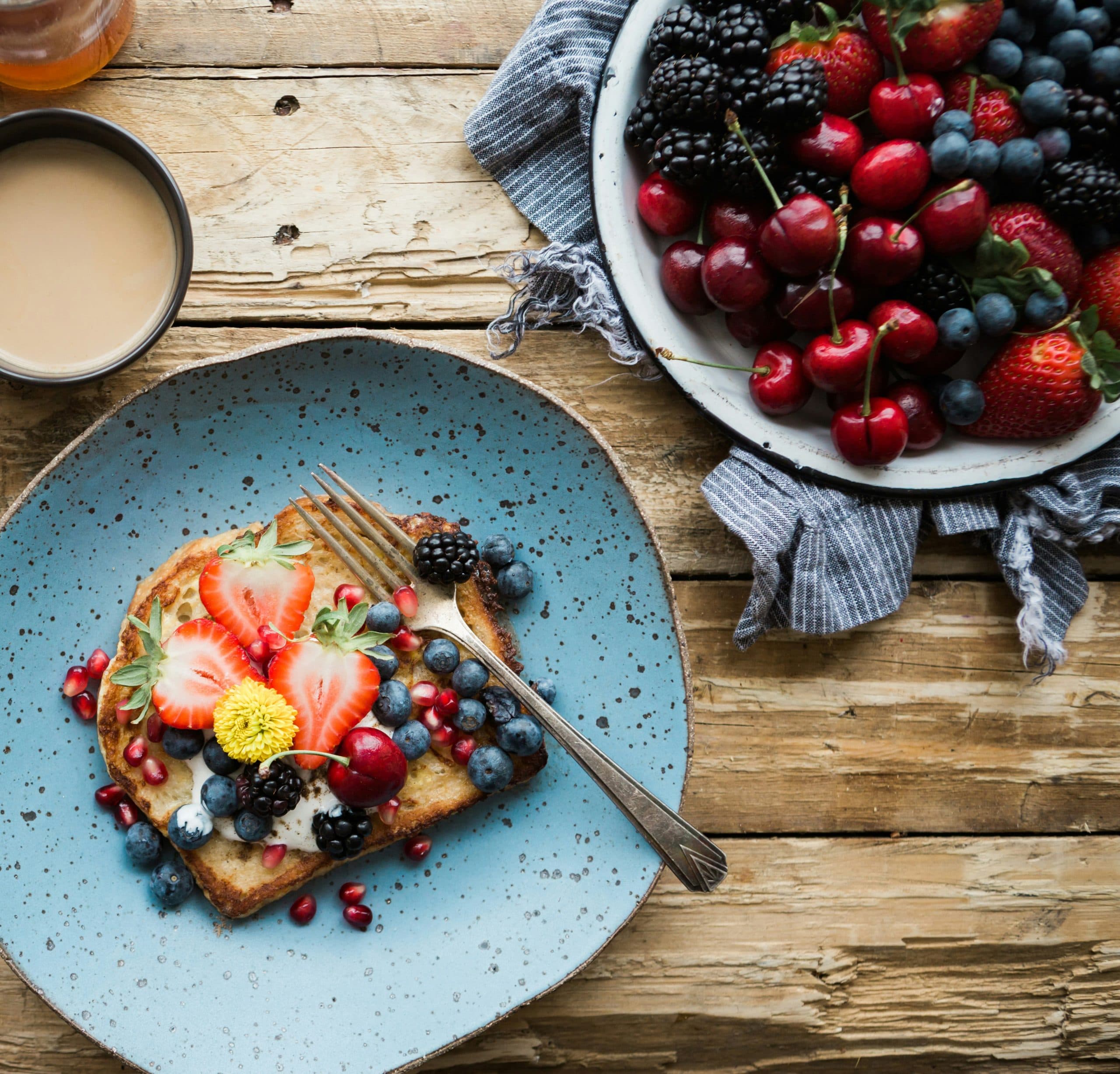 French toast topped with fresh berries beside a bowl of cherries and strawberries