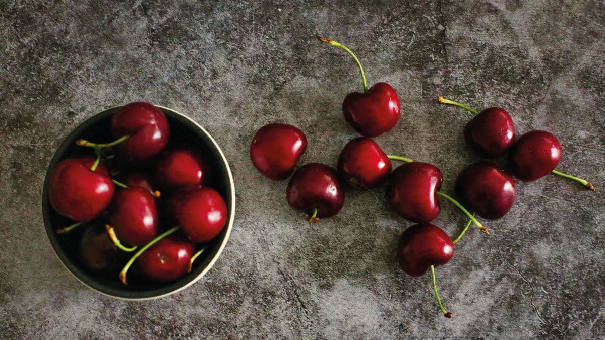 Bowl of fresh red cherries with more scattered beside it