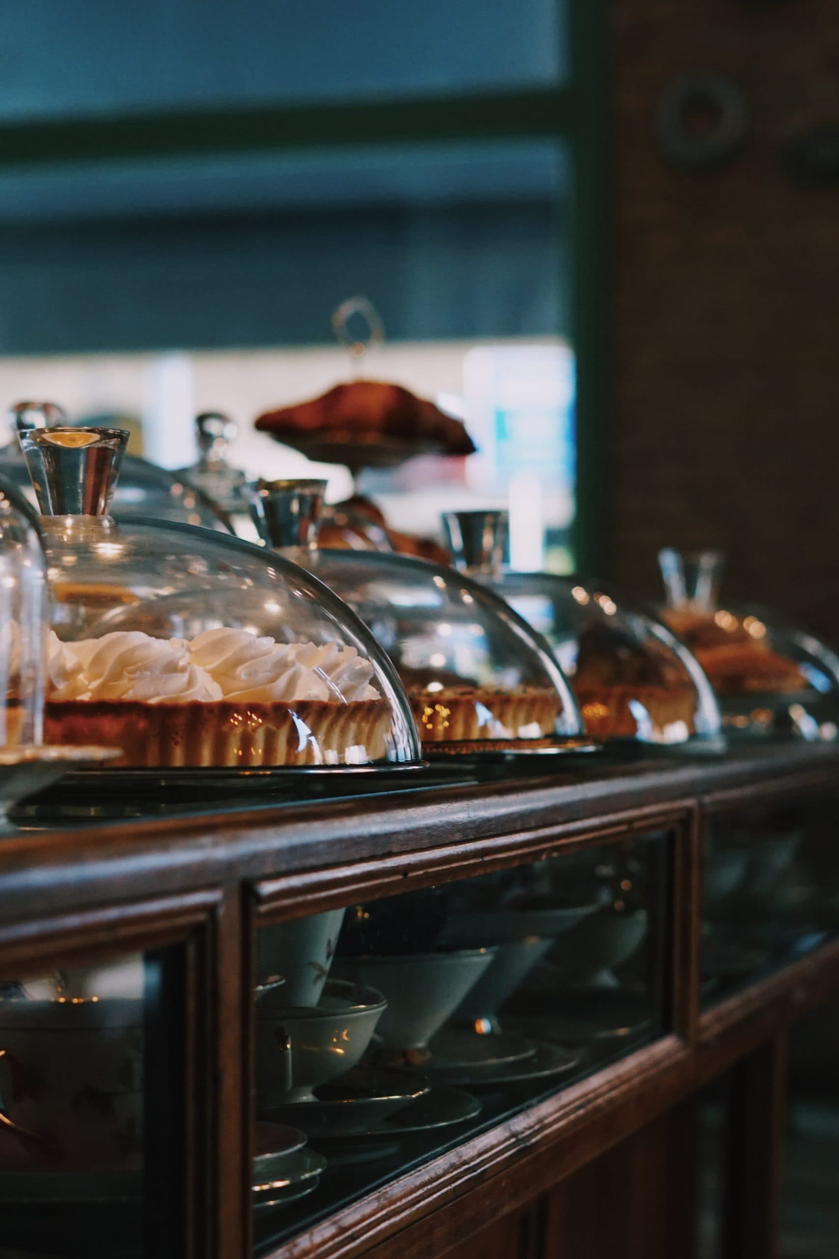 Cakes and tarts under glass domes on a wooden display counter