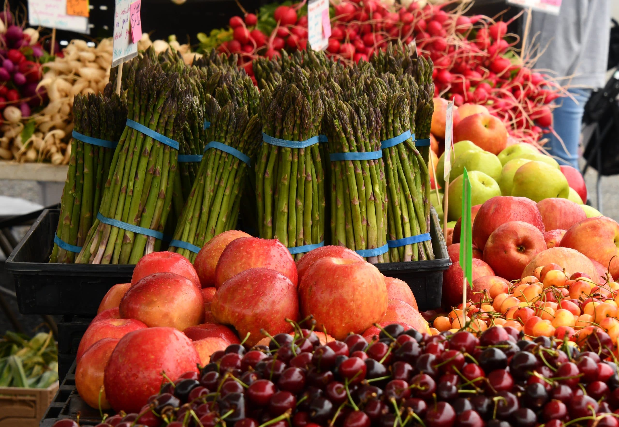 Market display of asparagus bunches, red apples and cherries