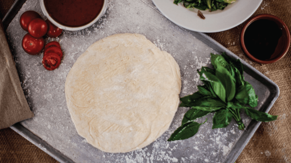 Pizza base on a tray with tomatoes, basil and sauces
